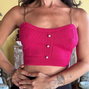 Título: Top Cropped de Tricô com Alças Douradas Descrição: Cropped em malha trabalhada que apresenta botões perolados centrais e delicadas alças em corrente metálica. A peça possui estrutura ajustada com barra canelada, sendo um elemento marcante para elevar produções noturnas quando combinada a peças de cintura alta.